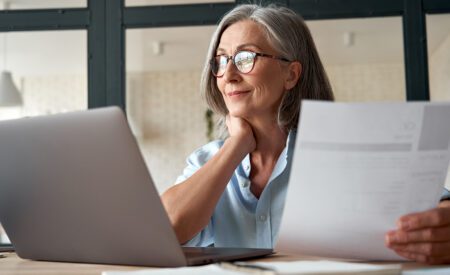 Woman holding a piece of paper and looking at her laptop