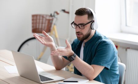 Man wearing glasses talking on headset and gesturing at computer