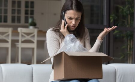 Woman with confused expression talking on phone while looking at open package box