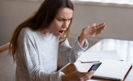 Angry woman looking at cellphone in her hand while yelling