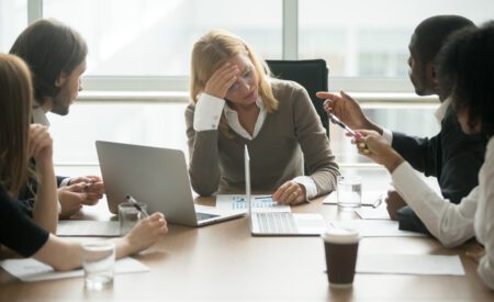 Group of professionals talking around a table while one woman looks stressed